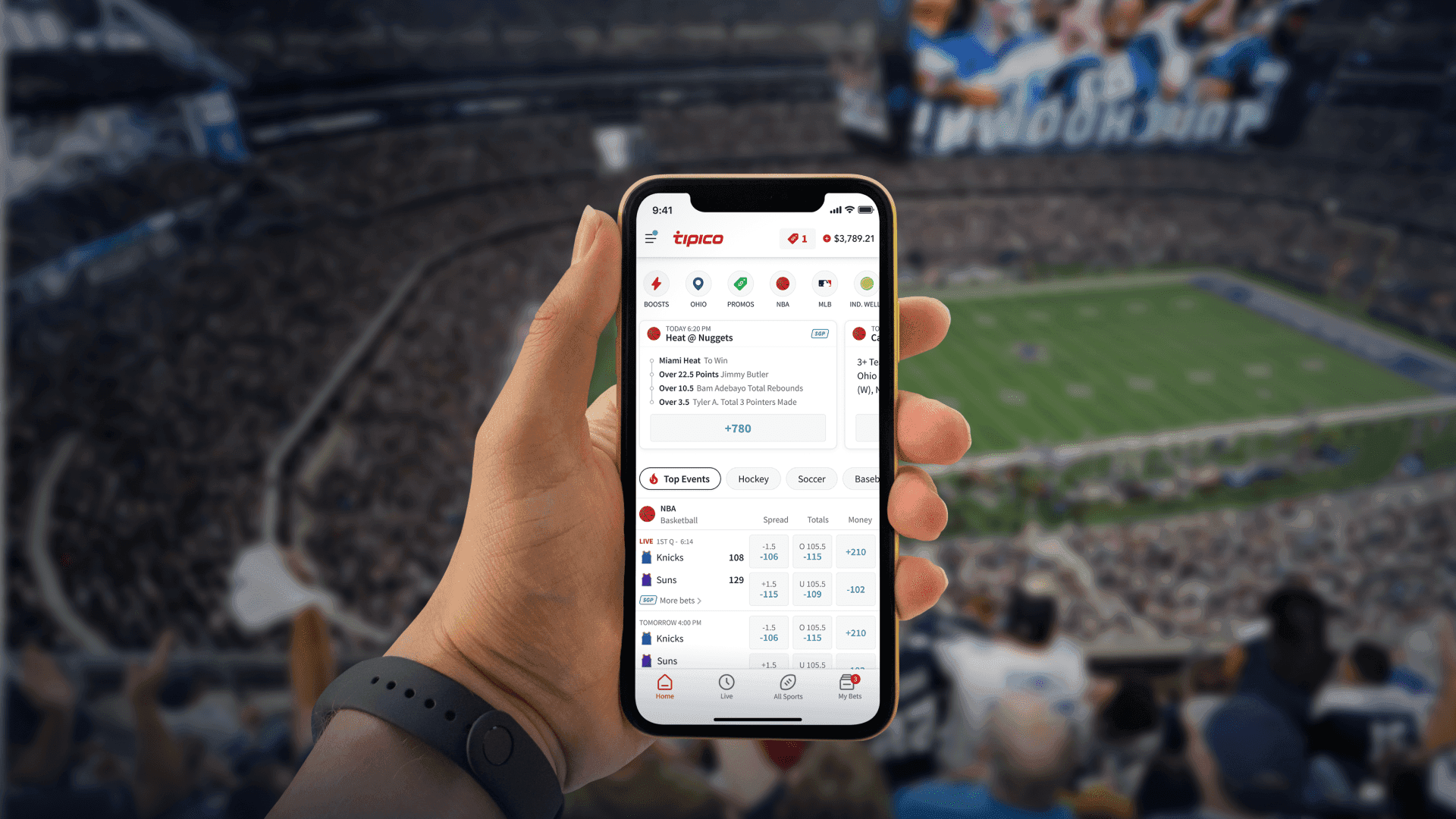 A hand holding the Tipico app in a packed football stadium